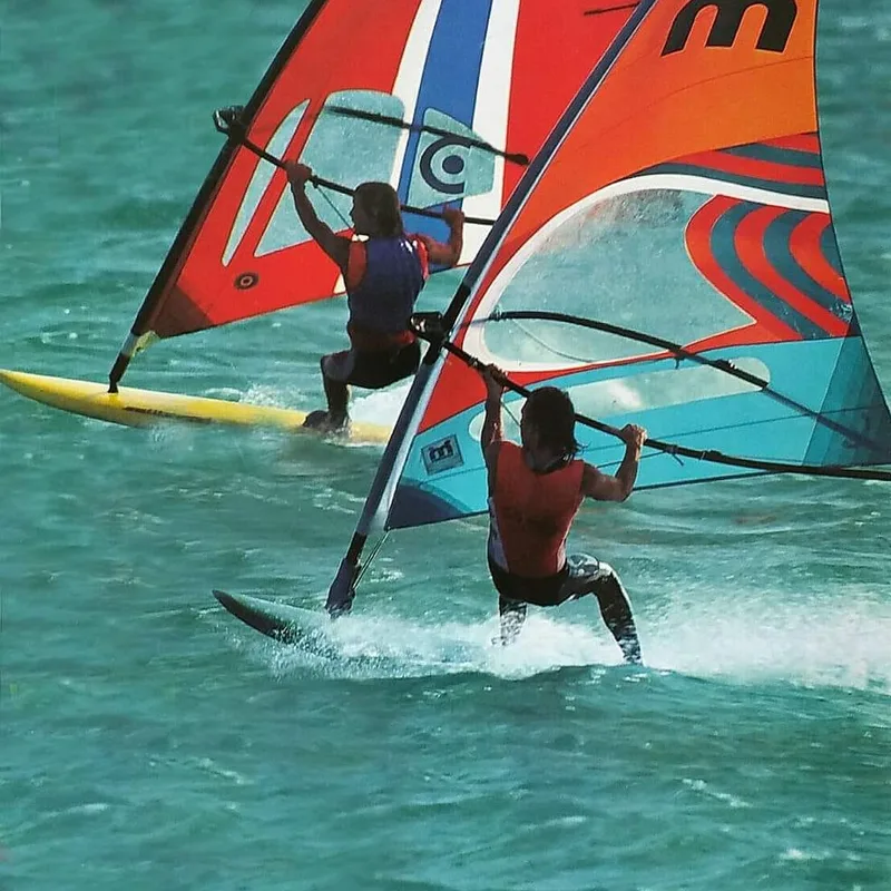 Twee windsurfers met zeilen uit de jaren tachtig op helder water